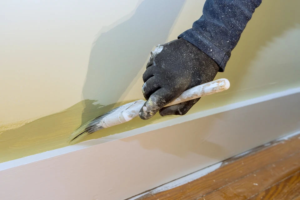 Un peintre mâle peint le mur de la maison avec une brosse à rouleaux